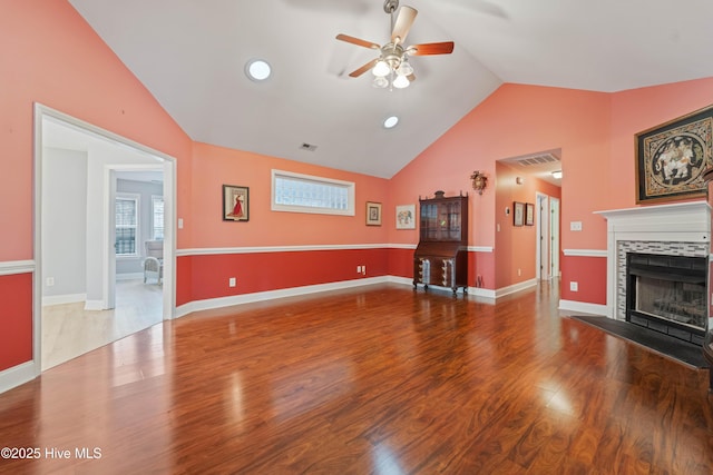 living room with ceiling fan, a tiled fireplace, lofted ceiling, and wood-type flooring