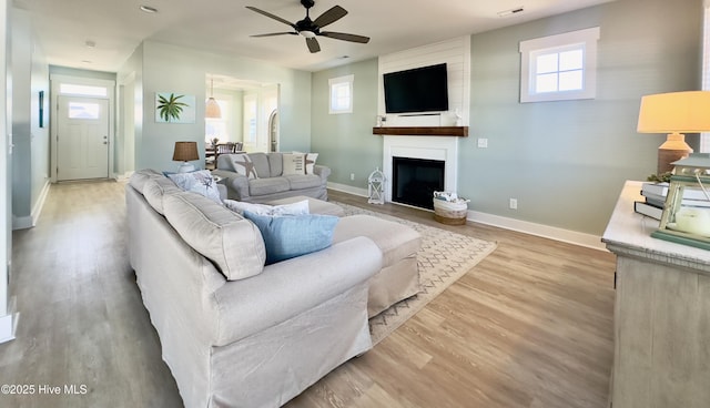 living room with ceiling fan, a large fireplace, and light wood-type flooring