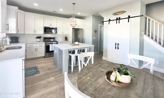 kitchen with sink, hanging light fixtures, stainless steel appliances, a kitchen island, and a barn door