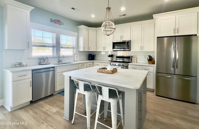 kitchen featuring sink, appliances with stainless steel finishes, white cabinetry, hanging light fixtures, and a kitchen island