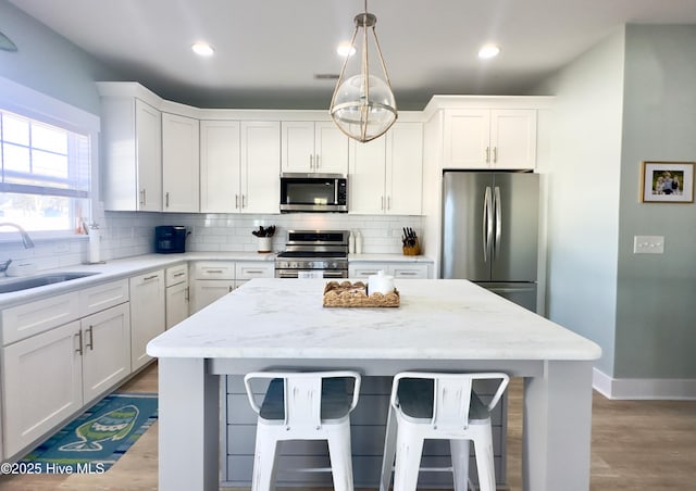 kitchen featuring white cabinetry, sink, a breakfast bar area, hanging light fixtures, and stainless steel appliances