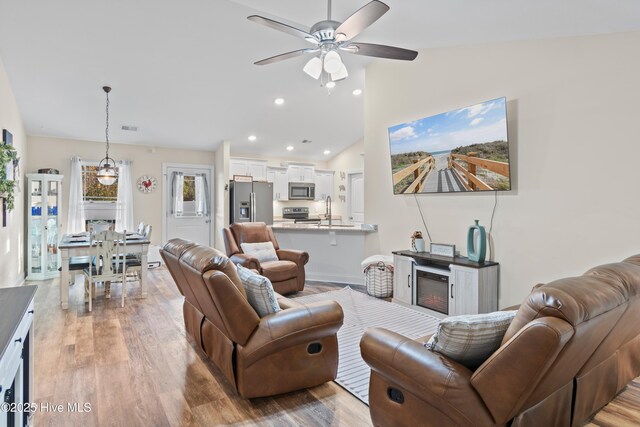 living room featuring sink, light wood-type flooring, vaulted ceiling, and ceiling fan