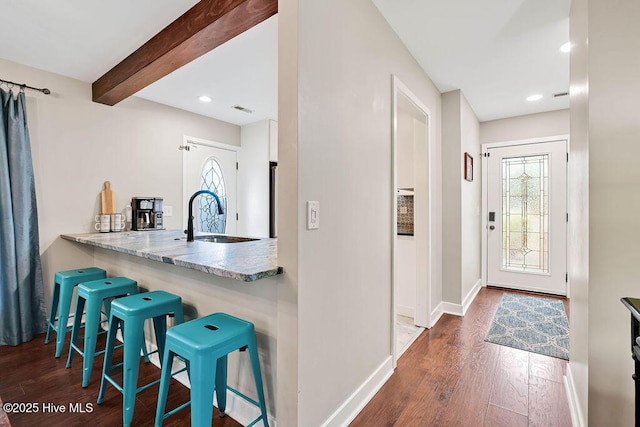 kitchen featuring sink, dark wood-type flooring, light stone countertops, a breakfast bar area, and beamed ceiling