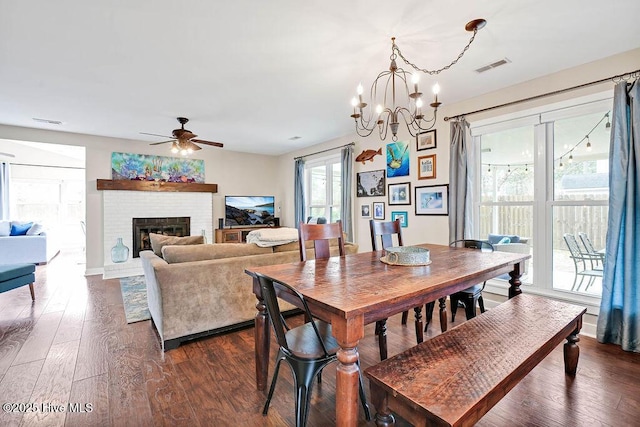 dining area featuring ceiling fan with notable chandelier, dark hardwood / wood-style floors, and a fireplace