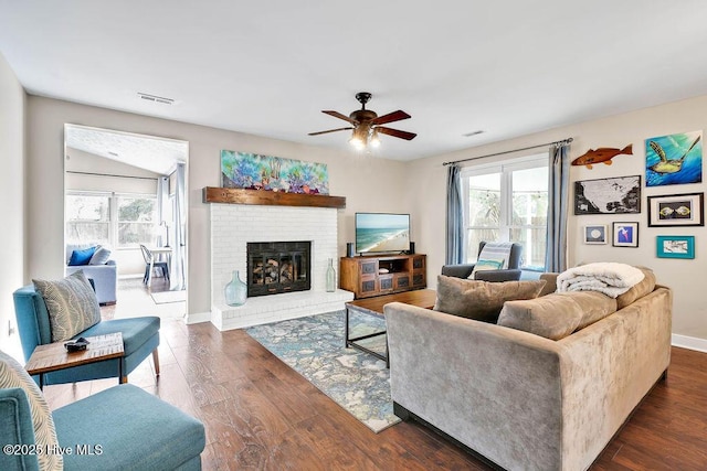 living room with ceiling fan, a brick fireplace, and dark hardwood / wood-style flooring