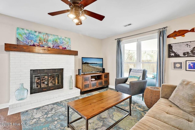 living room with a brick fireplace, wood-type flooring, and ceiling fan