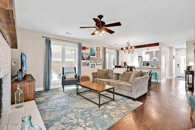 living room featuring sink, ceiling fan with notable chandelier, a brick fireplace, and dark hardwood / wood-style flooring