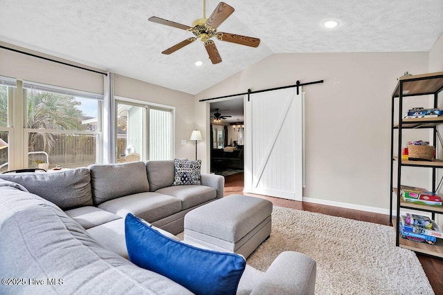 living room featuring wood-type flooring, vaulted ceiling, ceiling fan, a barn door, and a textured ceiling