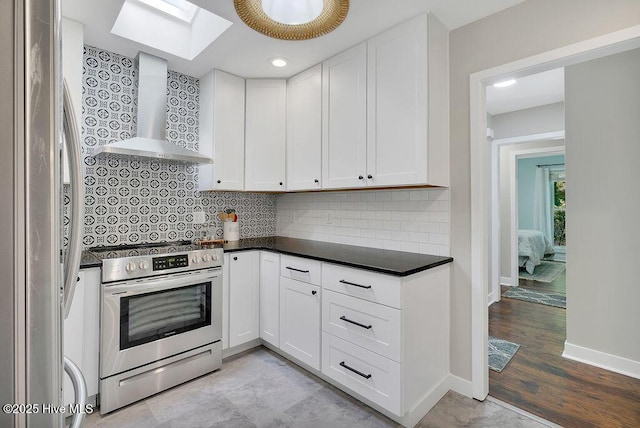 kitchen featuring a skylight, decorative backsplash, wall chimney range hood, white cabinets, and stainless steel appliances