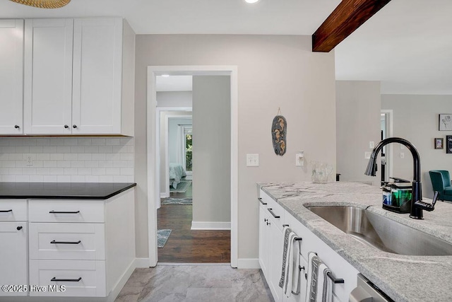 kitchen with sink, white cabinets, tasteful backsplash, light stone countertops, and beamed ceiling