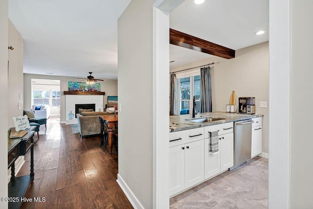 kitchen featuring stainless steel dishwasher, sink, white cabinets, beam ceiling, and a brick fireplace