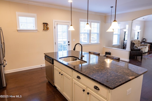 kitchen with appliances with stainless steel finishes, sink, dark stone countertops, hanging light fixtures, and a kitchen island with sink