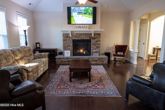 living room with lofted ceiling, dark wood-type flooring, ceiling fan, a stone fireplace, and ornate columns