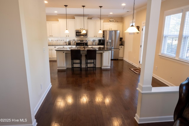 kitchen with a breakfast bar area, appliances with stainless steel finishes, white cabinetry, hanging light fixtures, and an island with sink