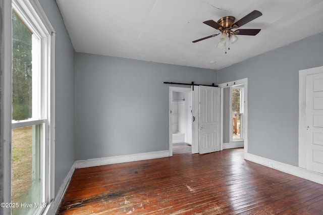 unfurnished room with ceiling fan, dark hardwood / wood-style flooring, and a barn door