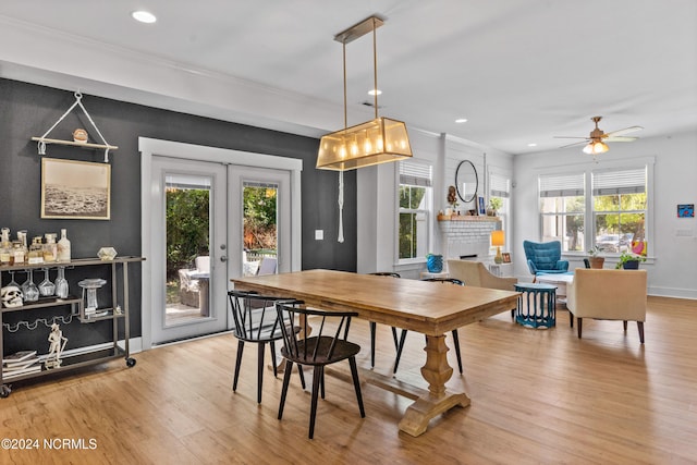 dining space with ceiling fan, a fireplace, ornamental molding, light hardwood / wood-style floors, and french doors