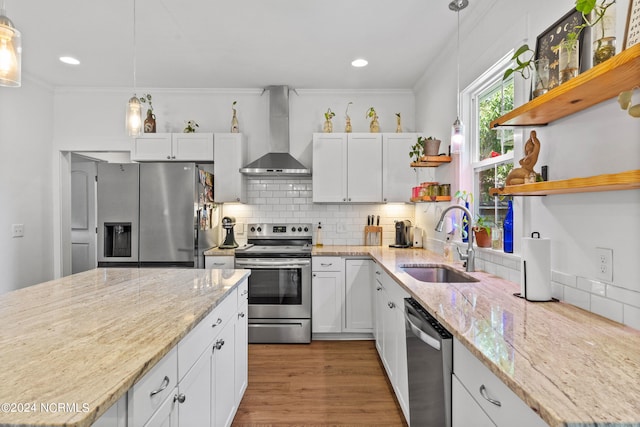 kitchen featuring stainless steel appliances, white cabinetry, decorative light fixtures, and wall chimney exhaust hood