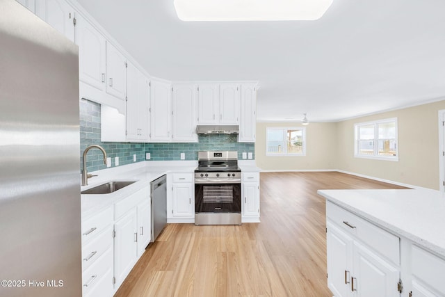 kitchen featuring sink, light wood-type flooring, white cabinets, stainless steel appliances, and backsplash