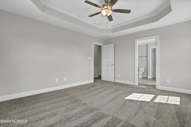 unfurnished bedroom with ceiling fan, crown molding, a tray ceiling, and ensuite bath