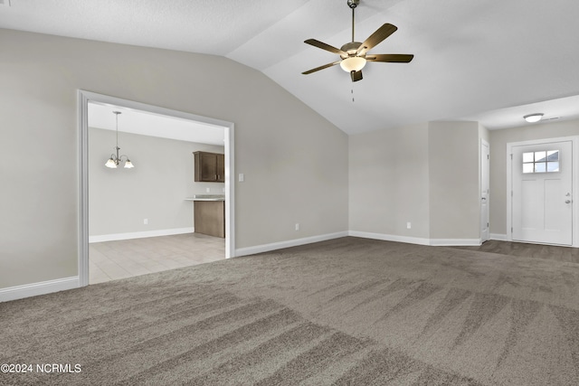 unfurnished living room featuring ceiling fan with notable chandelier, light colored carpet, and vaulted ceiling