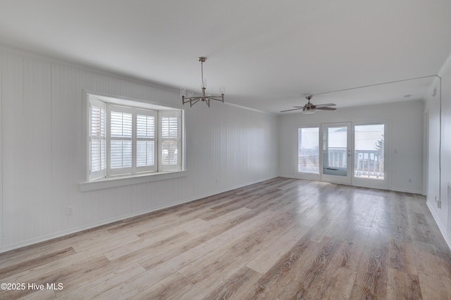 empty room with ceiling fan with notable chandelier, light wood-type flooring, and baseboards