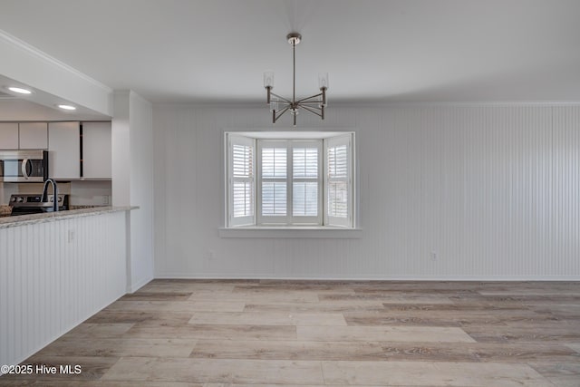 unfurnished dining area featuring a chandelier, light wood finished floors, and crown molding