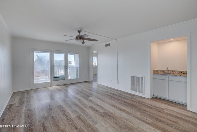 unfurnished living room featuring visible vents, crown molding, light wood-style flooring, and a sink