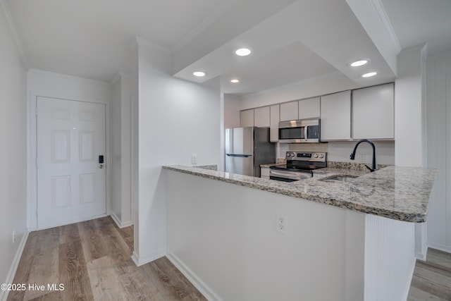 kitchen featuring light stone counters, light wood-style flooring, stainless steel appliances, a sink, and crown molding