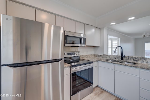 kitchen featuring light wood-style flooring, light stone countertops, stainless steel appliances, crown molding, and a sink