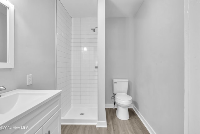 bathroom with hardwood / wood-style flooring, toilet, vanity, and a tile shower