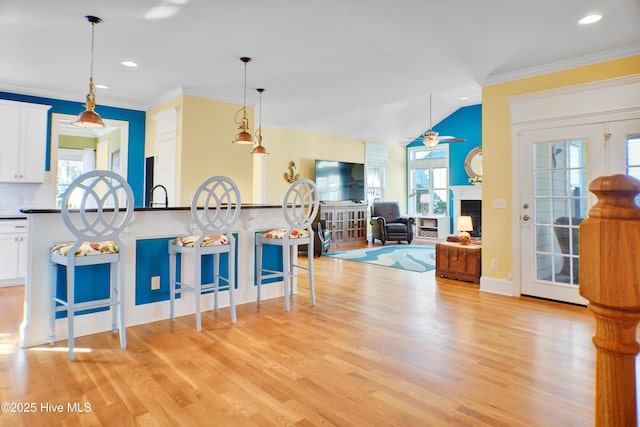 kitchen featuring decorative backsplash, white cabinets, decorative light fixtures, light hardwood / wood-style flooring, and a breakfast bar area