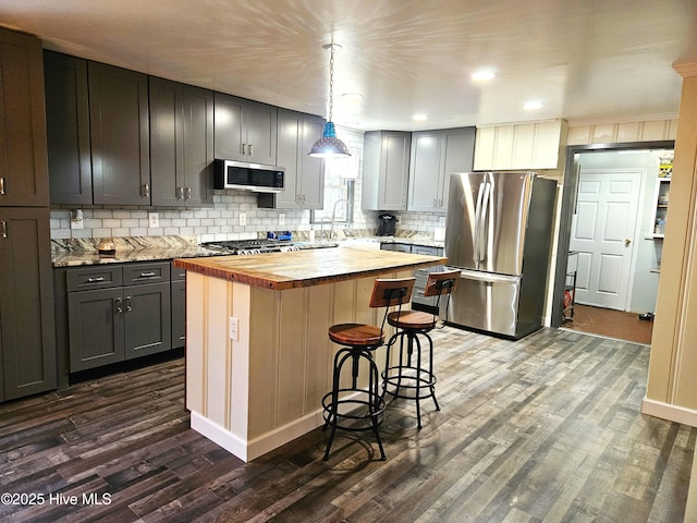 kitchen featuring a kitchen island, stainless steel appliances, hanging light fixtures, gray cabinets, and butcher block countertops