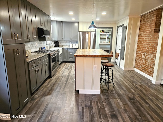 kitchen featuring appliances with stainless steel finishes, decorative light fixtures, butcher block countertops, a kitchen bar, and a center island