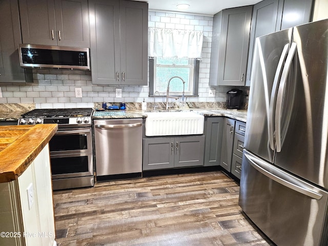 kitchen featuring wood-type flooring, appliances with stainless steel finishes, sink, gray cabinets, and butcher block counters