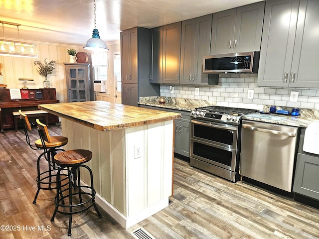 kitchen featuring hanging light fixtures, wooden counters, gray cabinetry, a center island, and stainless steel appliances