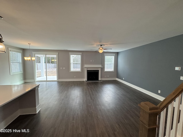 unfurnished living room featuring a wealth of natural light, ceiling fan with notable chandelier, and dark hardwood / wood-style flooring