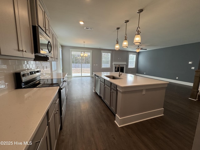 kitchen featuring sink, dark wood-type flooring, appliances with stainless steel finishes, hanging light fixtures, and an island with sink