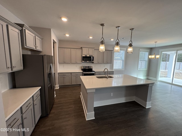 kitchen with sink, appliances with stainless steel finishes, a kitchen island with sink, hanging light fixtures, and gray cabinetry