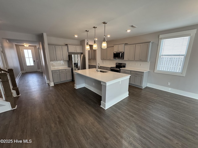 kitchen featuring sink, dark wood-type flooring, appliances with stainless steel finishes, an island with sink, and decorative light fixtures