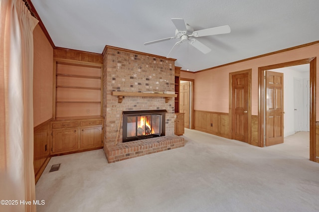 unfurnished living room featuring crown molding, ceiling fan, light colored carpet, a fireplace, and wood walls