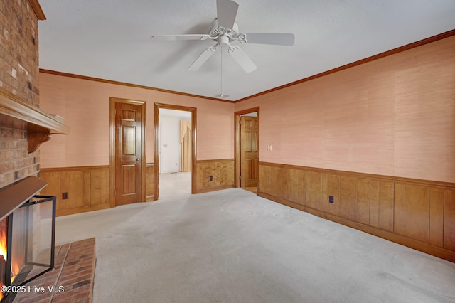 unfurnished living room featuring light carpet, ceiling fan, crown molding, and a fireplace