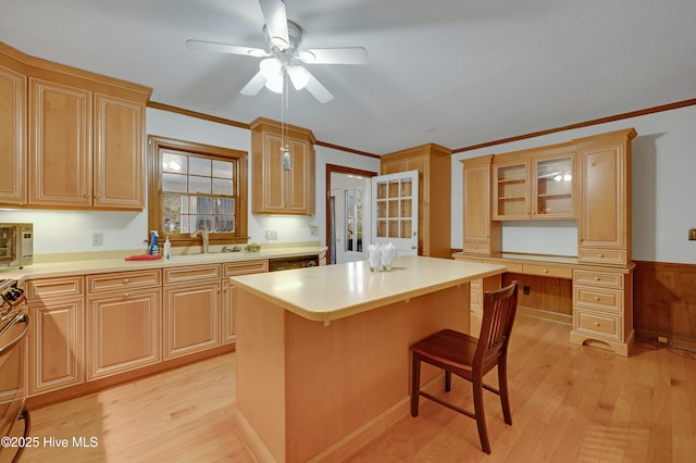 kitchen with light brown cabinets, a kitchen island, wood walls, light hardwood / wood-style floors, and built in desk