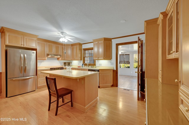 kitchen featuring a center island, a kitchen bar, light brown cabinetry, stainless steel refrigerator, and ornamental molding