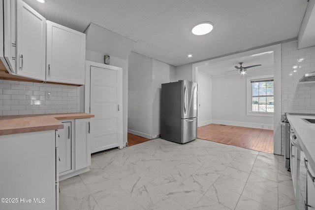 kitchen featuring butcher block countertops, stainless steel refrigerator, white cabinetry, decorative backsplash, and ceiling fan