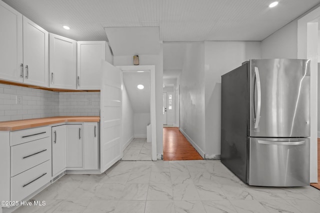 kitchen featuring tasteful backsplash, stainless steel fridge, butcher block countertops, and white cabinets