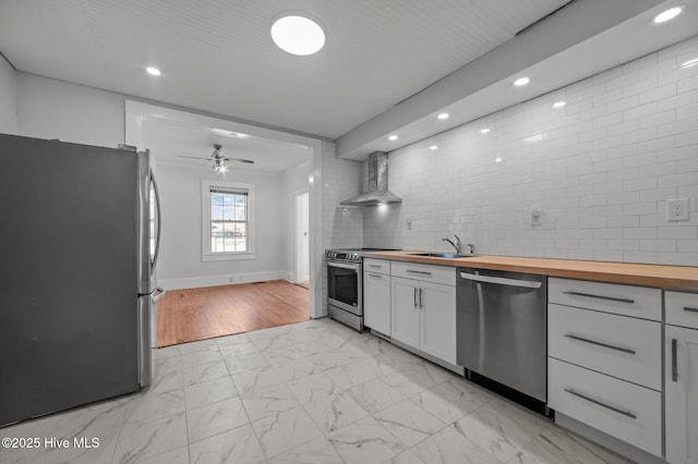 kitchen featuring butcher block countertops, wall chimney range hood, white cabinetry, stainless steel appliances, and tasteful backsplash