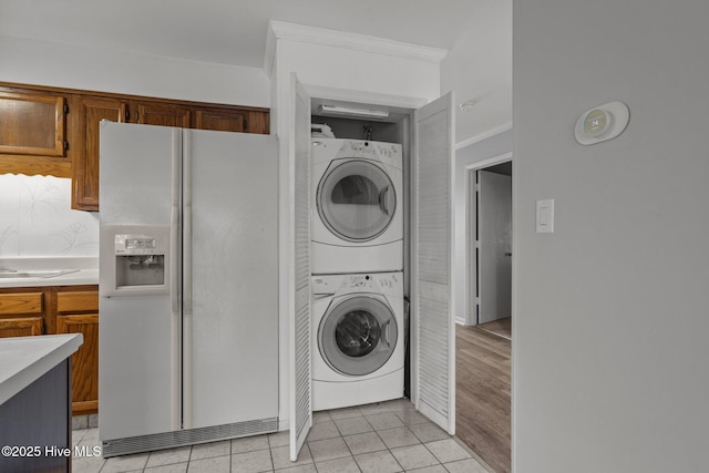 laundry room with ornamental molding, stacked washer / drying machine, sink, and light tile patterned floors