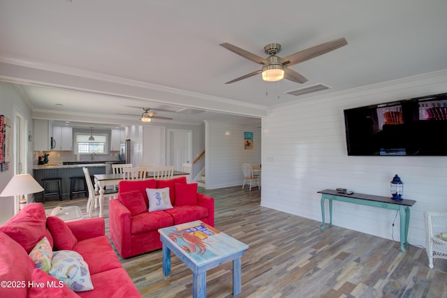 living room with ceiling fan, hardwood / wood-style floors, ornamental molding, and wooden walls