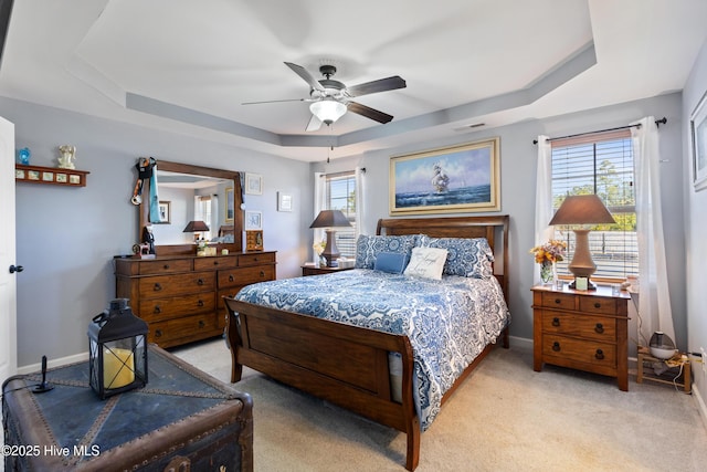 carpeted bedroom with a raised ceiling and ceiling fan