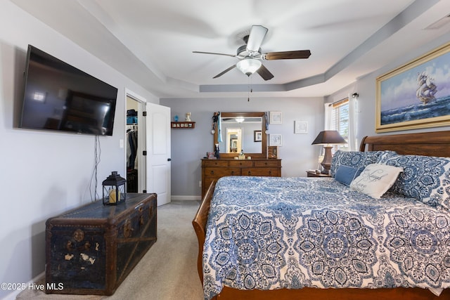 carpeted bedroom with a raised ceiling, a walk in closet, and ceiling fan